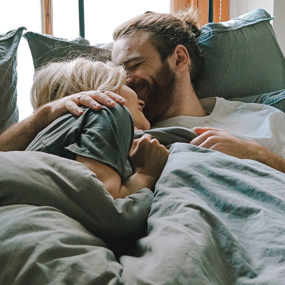 Couple cuddling and smiling in bed together as the sun shines